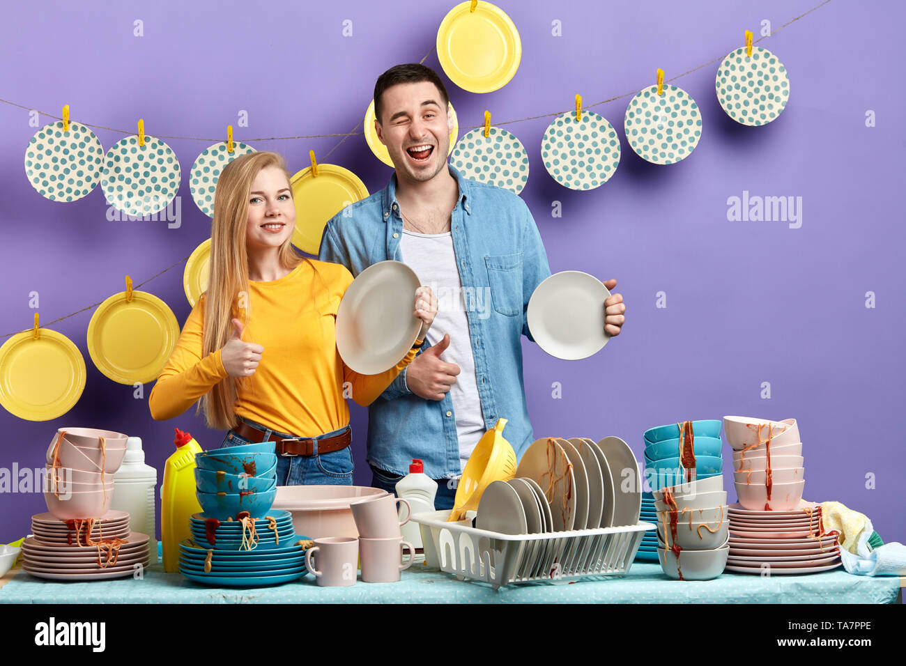 Young smiling woman and man showing thumbs up to the camera, effective good dishwashing liquid for dirty tablewear Stock Photo