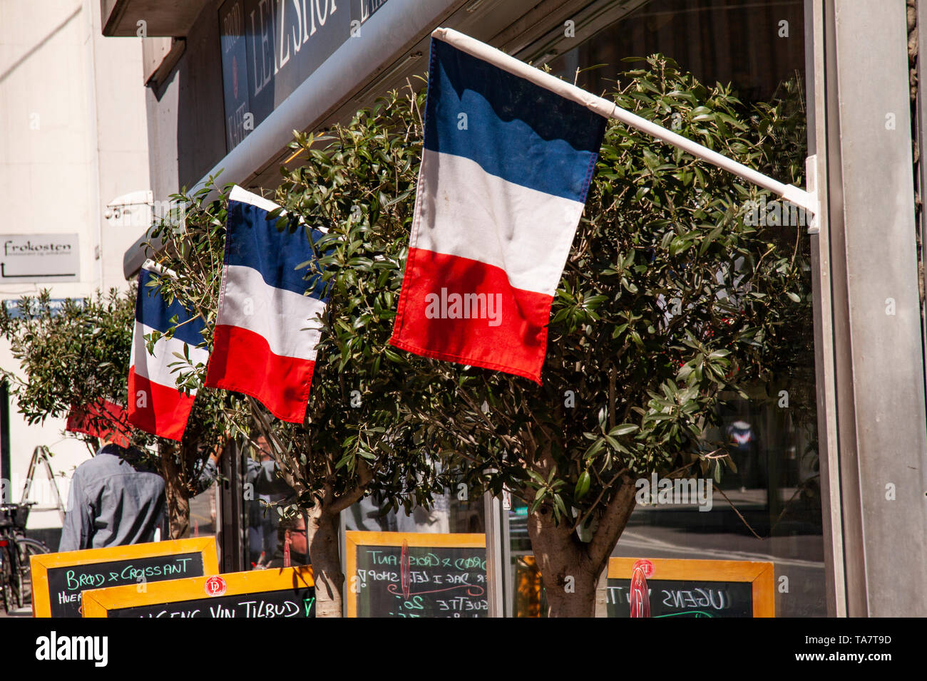 French cafe terrace flies the tri-colors in front of restaurant and shop.  Outside image with chairs, tables, billbords and olive trees Stock Photo -  Alamy