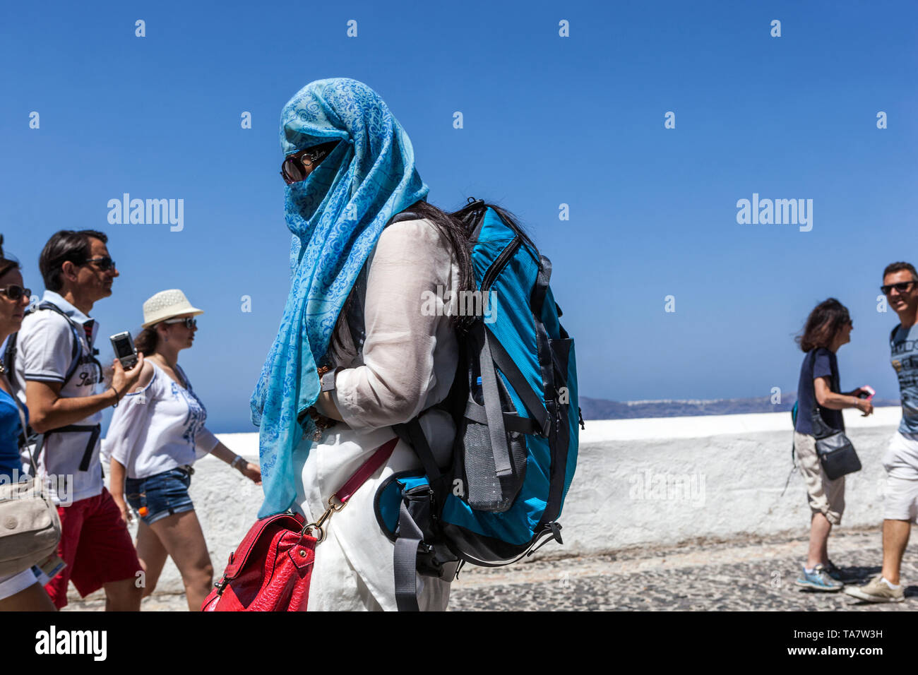 Arab woman covered in a blue scarf with a backpack on a walk. The terrace above the sea, Santorini tourist Greek Islands Greece Europe hidden woman Stock Photo