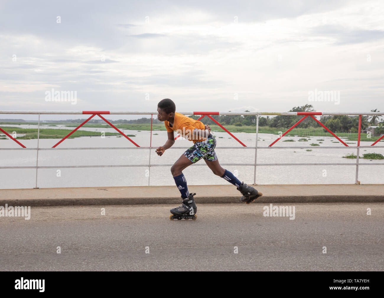 African boy roller skating on the bridge over Ouladine lagoon, Sud-Comoé, Grand-Bassam, Ivory Coast Stock Photo