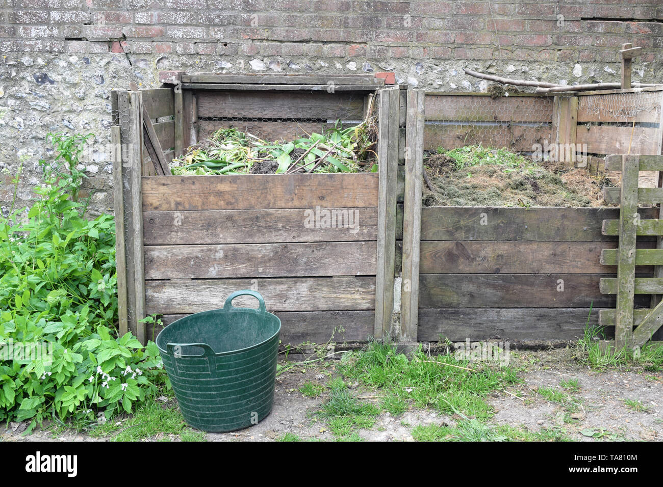 Large garden compost structure made of wood against a brick wall, recycle waste plants and food Stock Photo