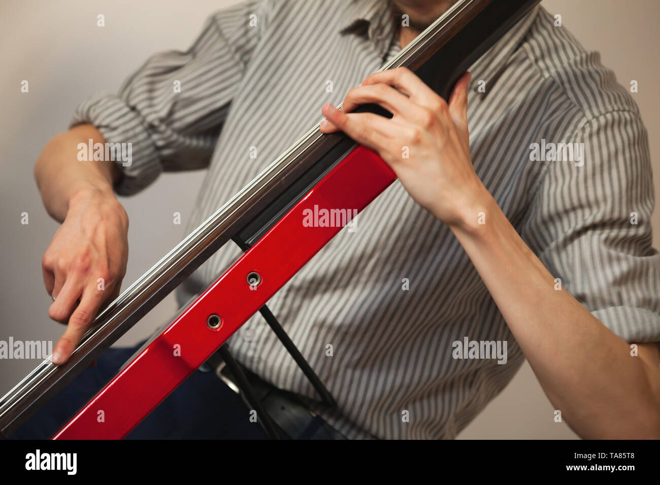 Hands of a man playing red modern electric contrabass in musical studio Stock Photo