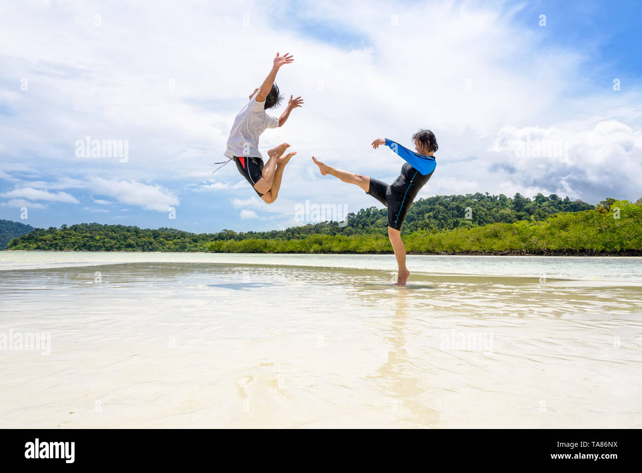 Happy asian couple play fun activity together woman show the teasing position, kicking a man to bounce far away on the beach of Ko Ra Wi near Ko Lipe  Stock Photo