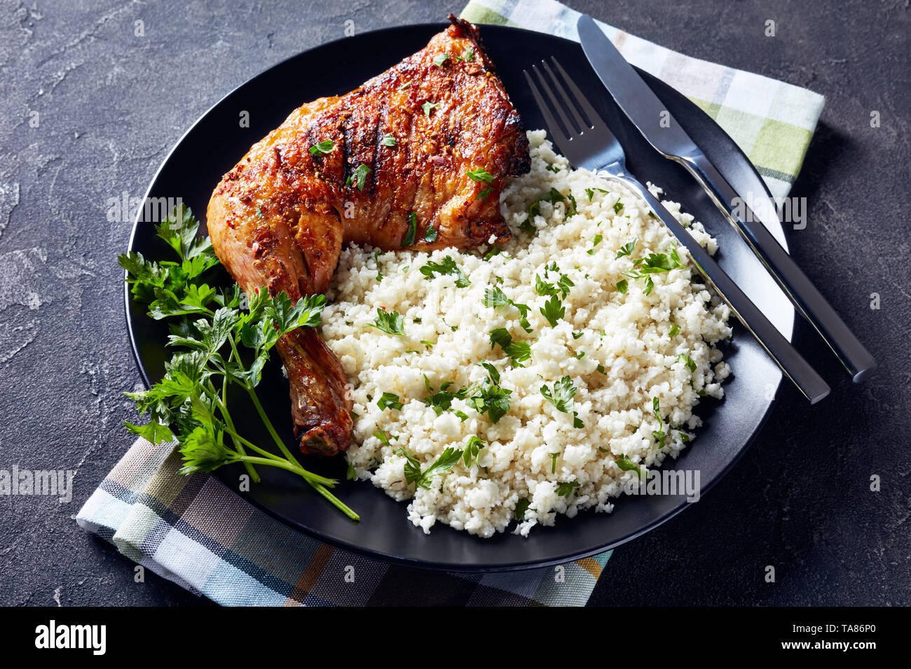 Crispy grilled Chicken Leg Quarter served with Cauliflower rice or couscous on a black plate on