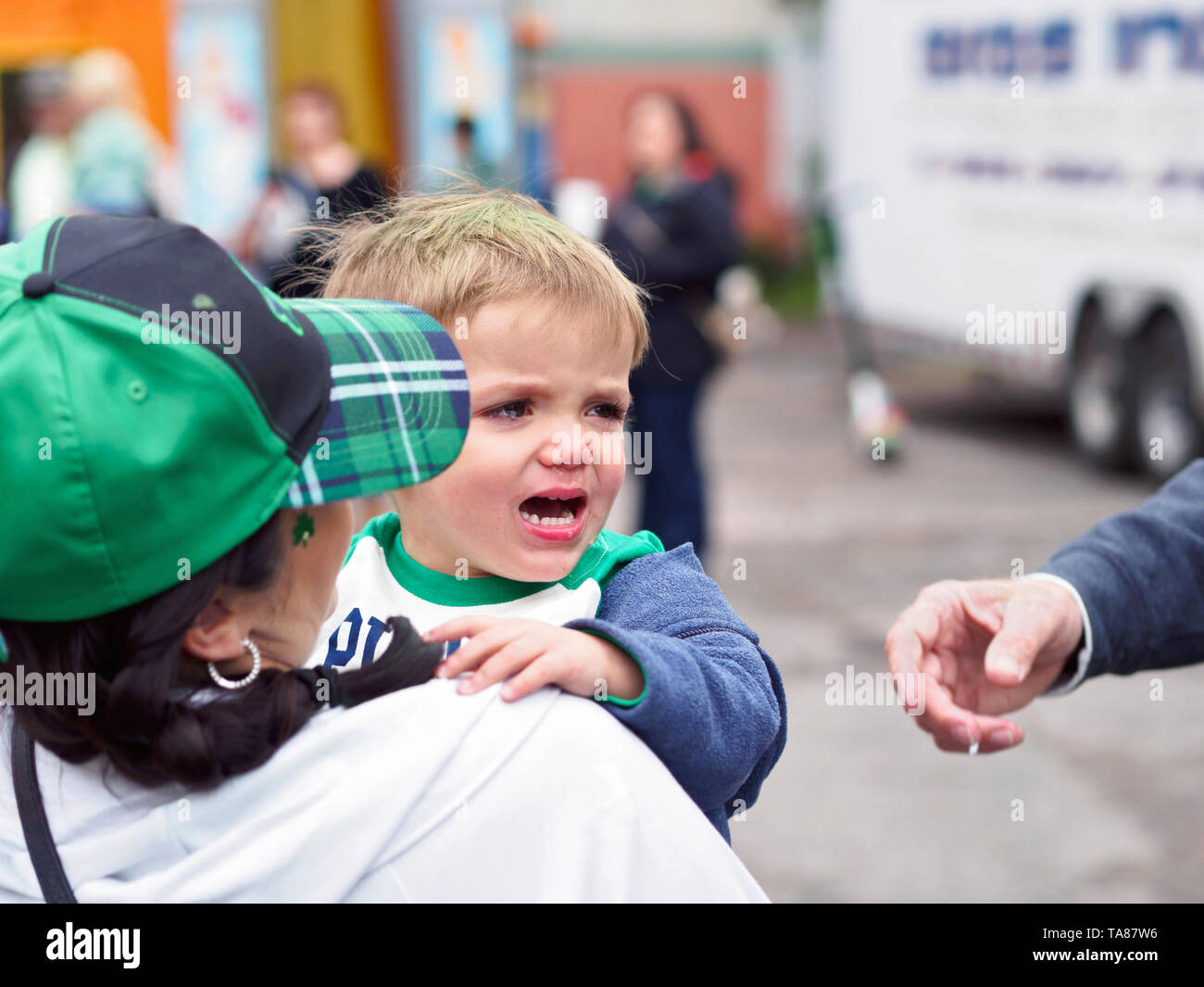 A little boy is crying as his mother holds him at the 2019 St. Patrick's Day Block Party in Corpus Christi, Texas USA. Stock Photo