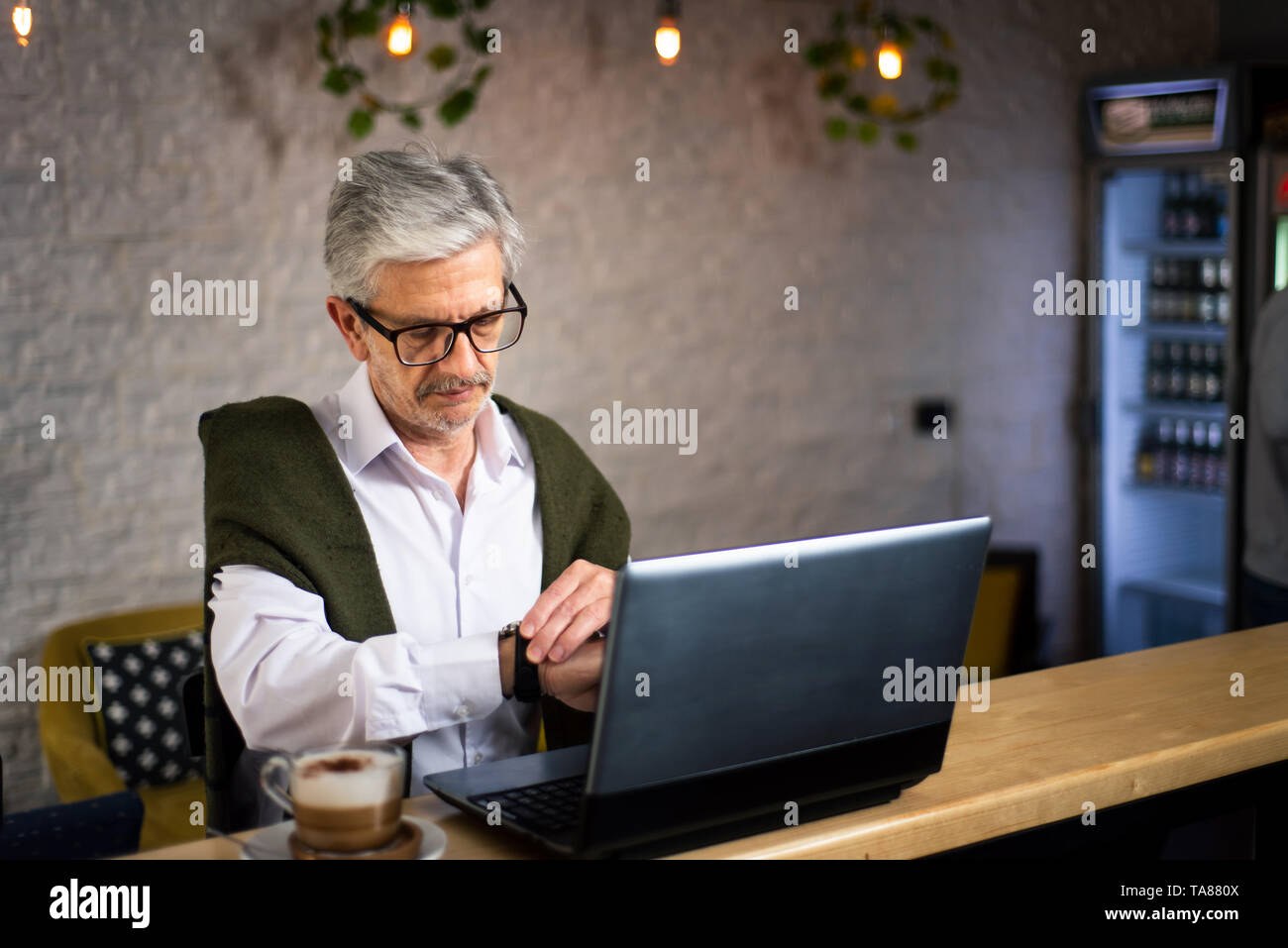 Senior man checking time while using laptop and having coffee in the bar Stock Photo