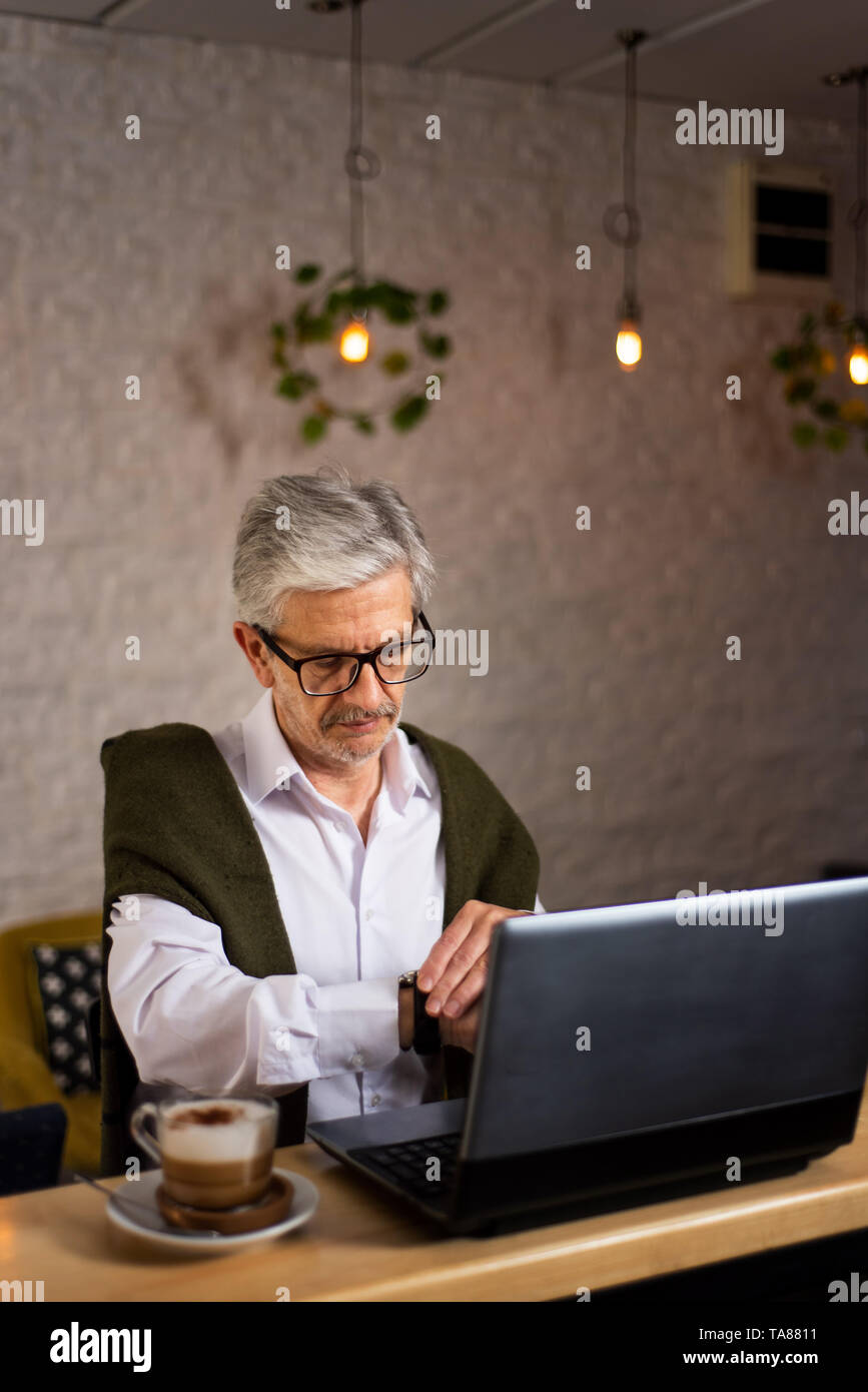 Senior man checking time while using laptop and having coffee in the bar Stock Photo