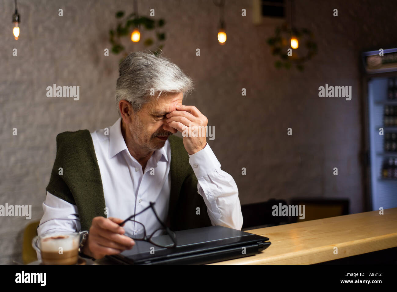 Tired senior man with laptop sitting in the bar Stock Photo