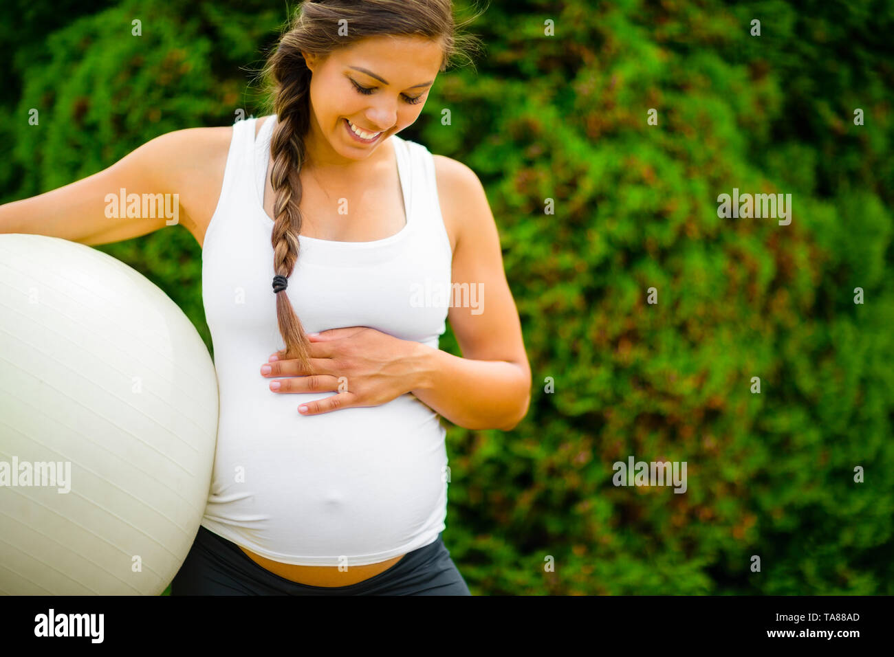 Pregnant Woman Touching Abdomen While Holding Fitness Ball In Park Stock Photo
