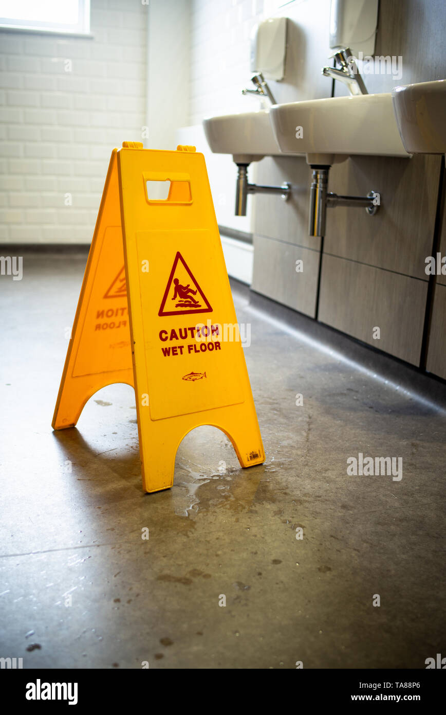 Caution wet floor safety stand up yellow warning sign in a toilet Stock