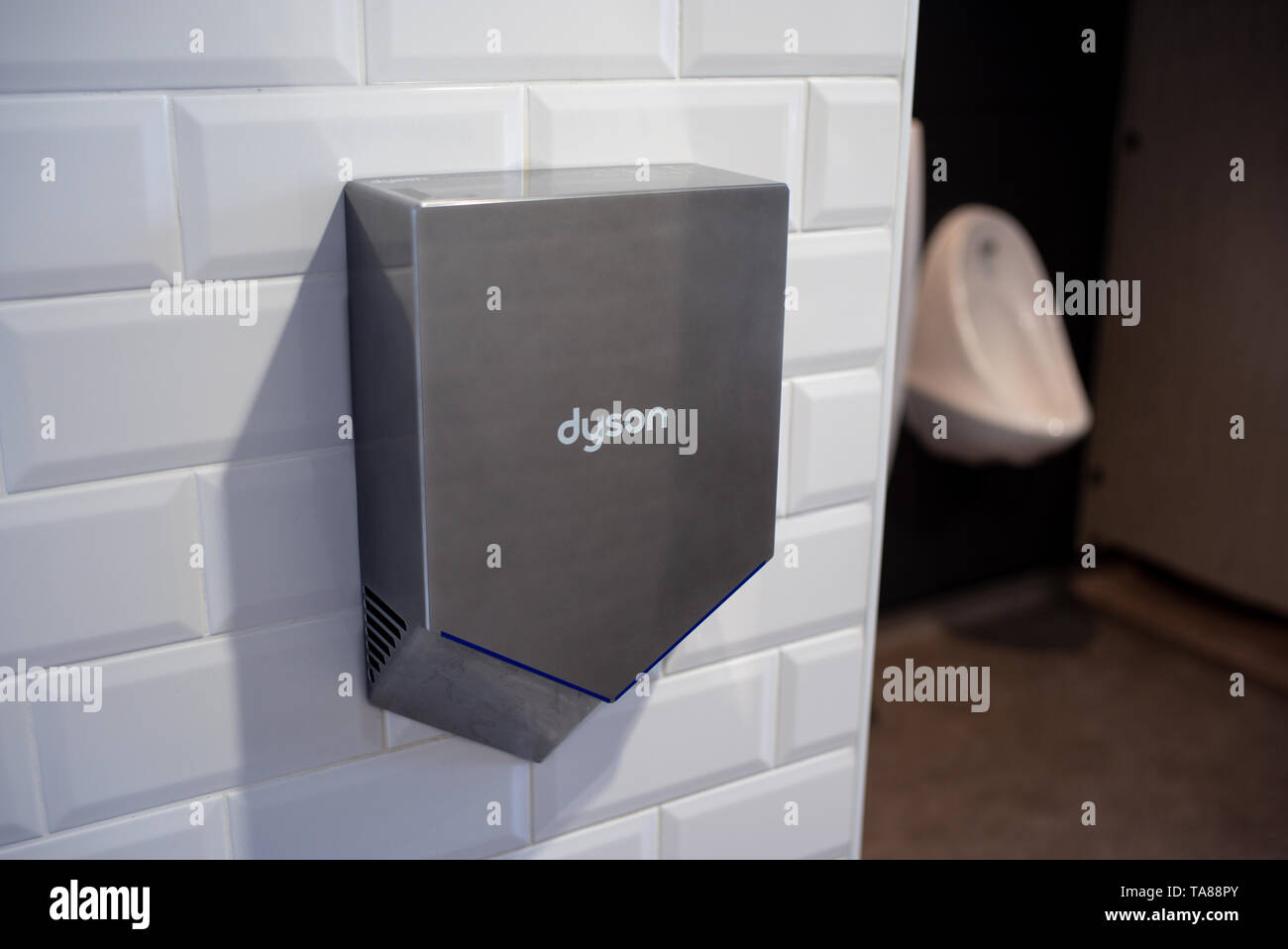 An angled Dyson hand dryer in a public toilet with a urinal in the