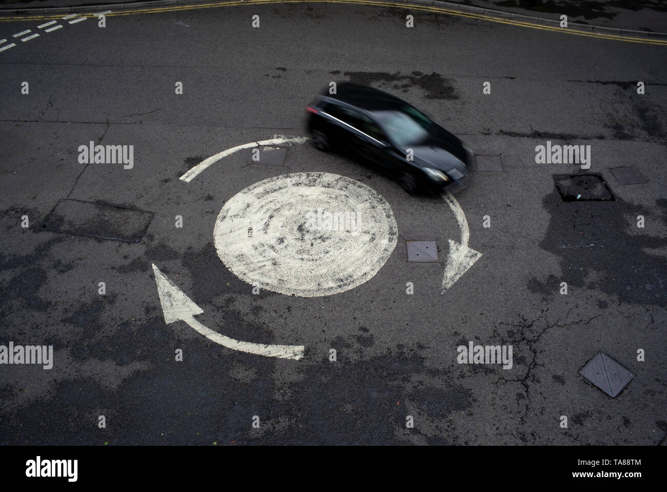 Aerial view of a painted arrowed roundabout with a single car going around. Could be used as an analogy or concept as being lost or going in circles. Stock Photo