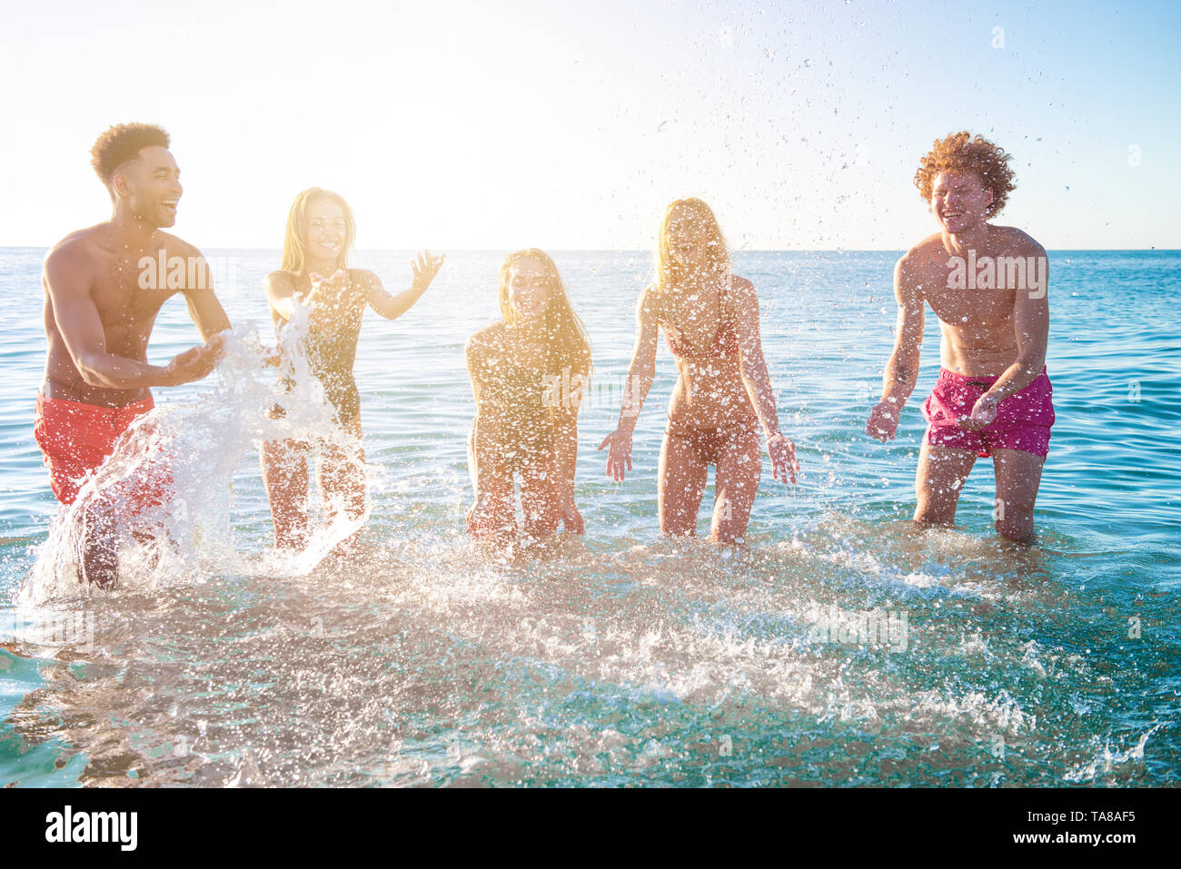 Group of happy friends having fun with water sea at ocean beach at dawn Stock Photo