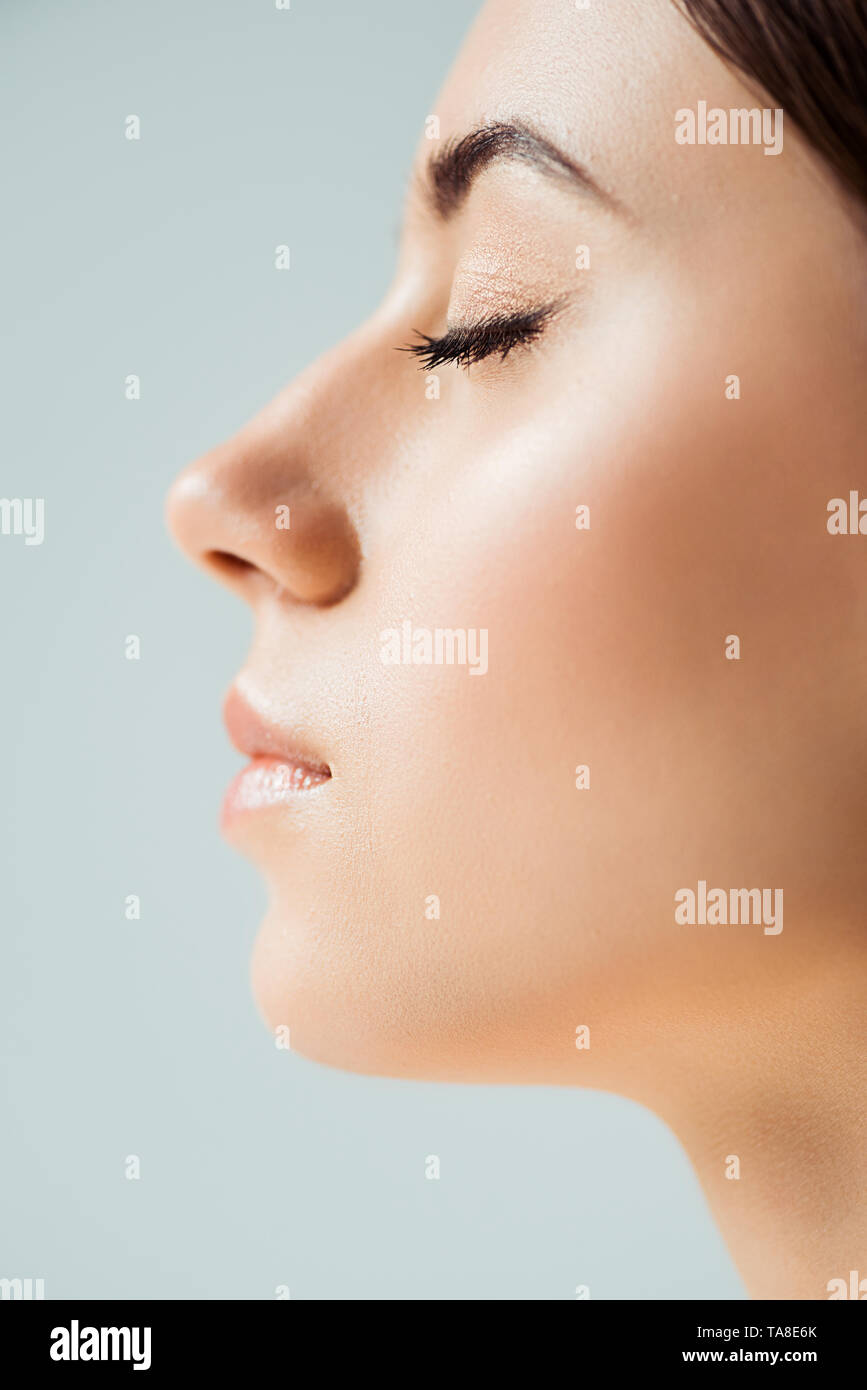 profile of young woman with closed eyes, shiny lips and golden eye shadow isolated on grey Stock Photo