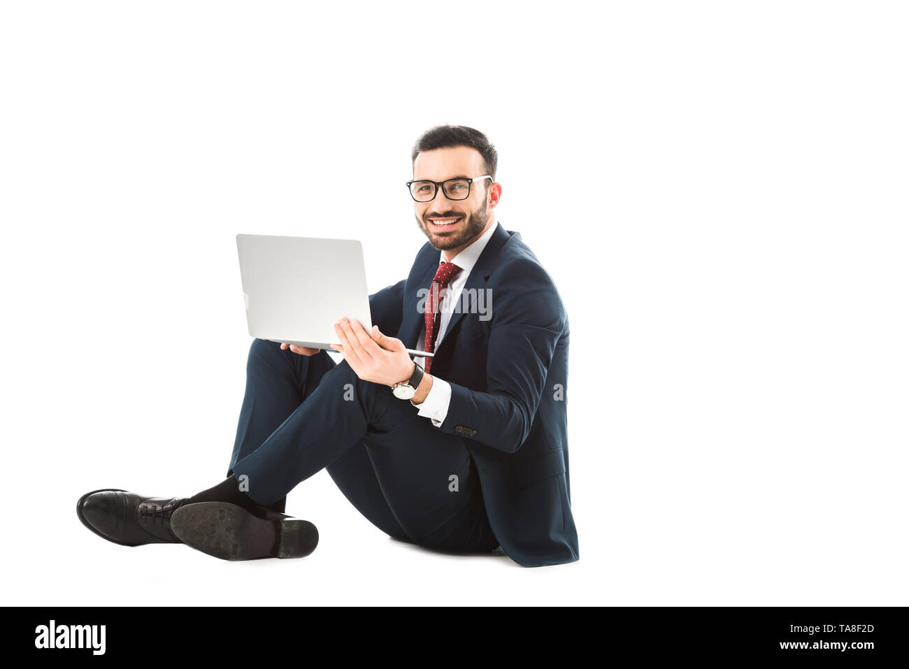 smiling businessman looking at camera while sitting and using laptop on ...