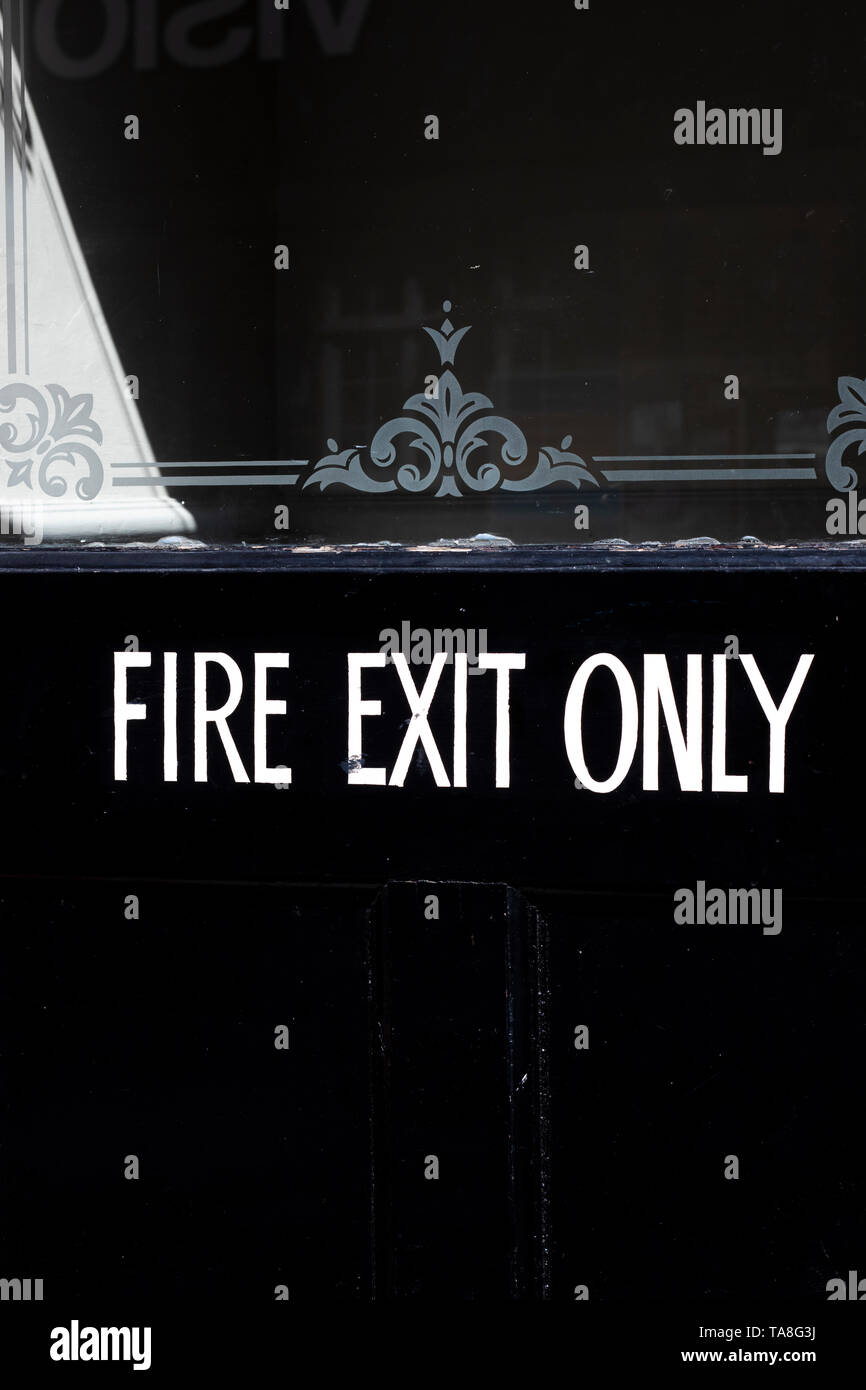 emergency fire exit only sign on black painted timber door to retail
