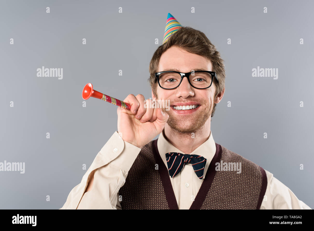 happy man in glasses and party cap holding party horn isolated on grey ...