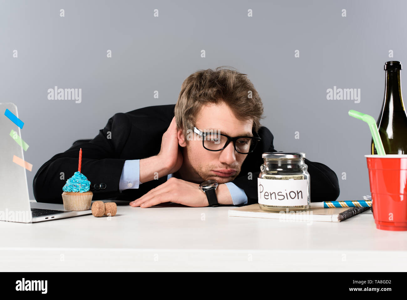 sad  businessman in glasses looking at pension moneybox isolated on grey Stock Photo