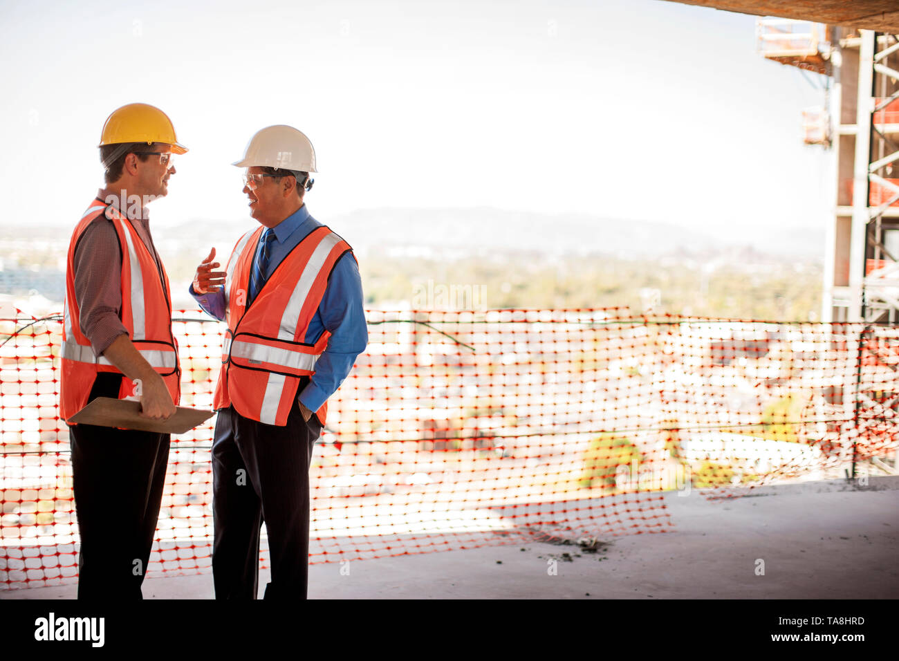 Two executives in safety gear talk on construction site. Stock Photo