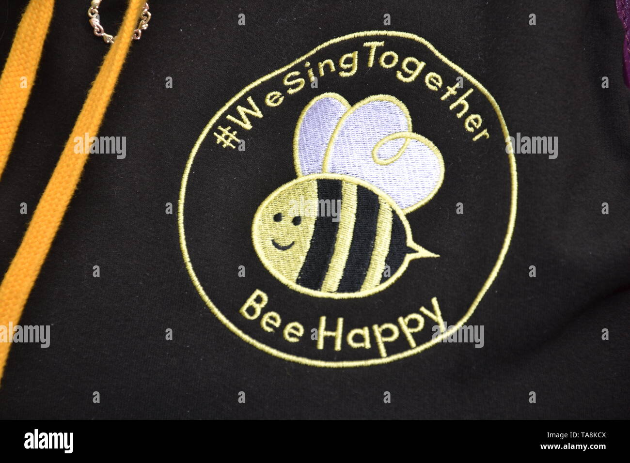 22nd May, 2019. Second Anniversary Commemoration of the Manchester Arena Bomb terror attack which left 22 people dead: members of the Manchester Survivors Choir sing in St Ann's Square, Manchester. uk. Photo shows the logo members of the choir all wear on their jackets. The Bee is a symbol of Manchester, uk. Stock Photo
