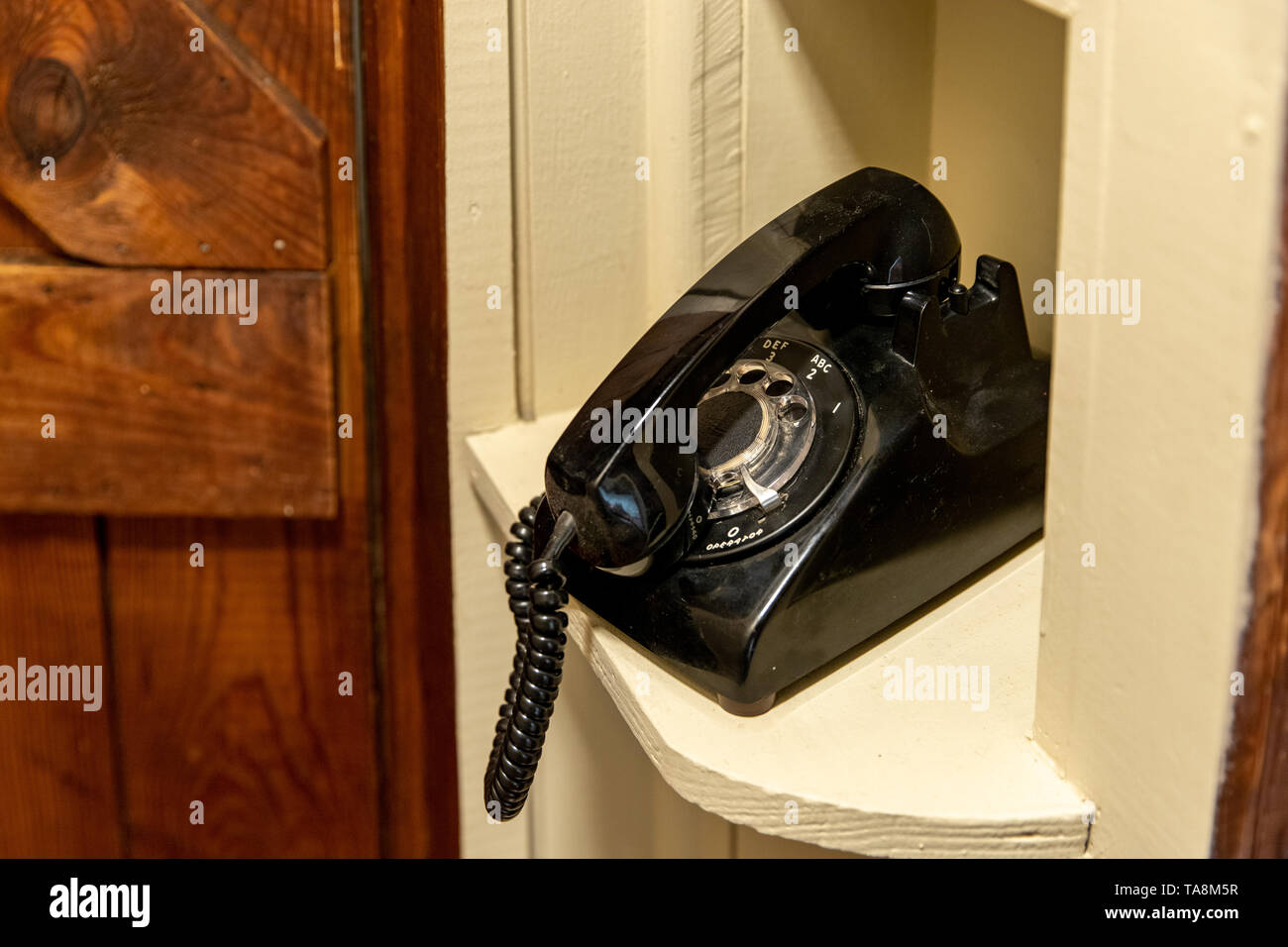 Old black rotary telephone, in on hold position, sitting, in hallway phone nook Stock Photo
