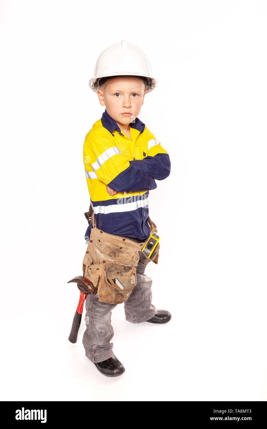 Young blond caucasian boy arms folded or on his hips role playing as an angry construction worker in a yellow and blue hi-viz shirt, boots, white hard Stock Photo