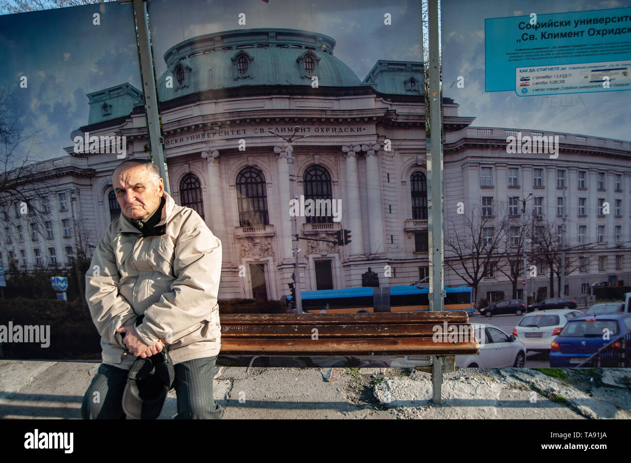 A Bulgarian man waits at a bus stop with a picture of Sofia University behind him. Bulgaria with an ageing population is the fastest shrinking country Stock Photo