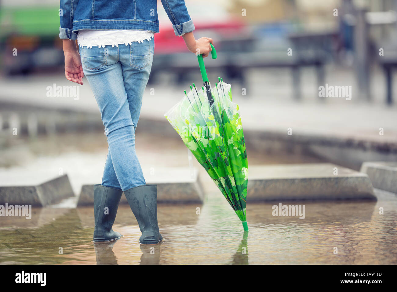 Young pre-teen girl stands with an umbrella in puddle after spring or summer rain. Stock Photo