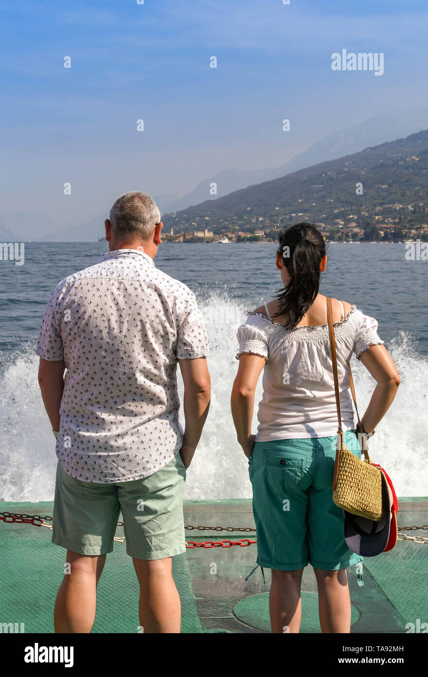 GARDA, LAKE GARDA, ITALY - SEPTEMBER 2018: Two people standing on the front of a  passenger ferry on a journey across Lake Garda with waves and spray. Stock Photo