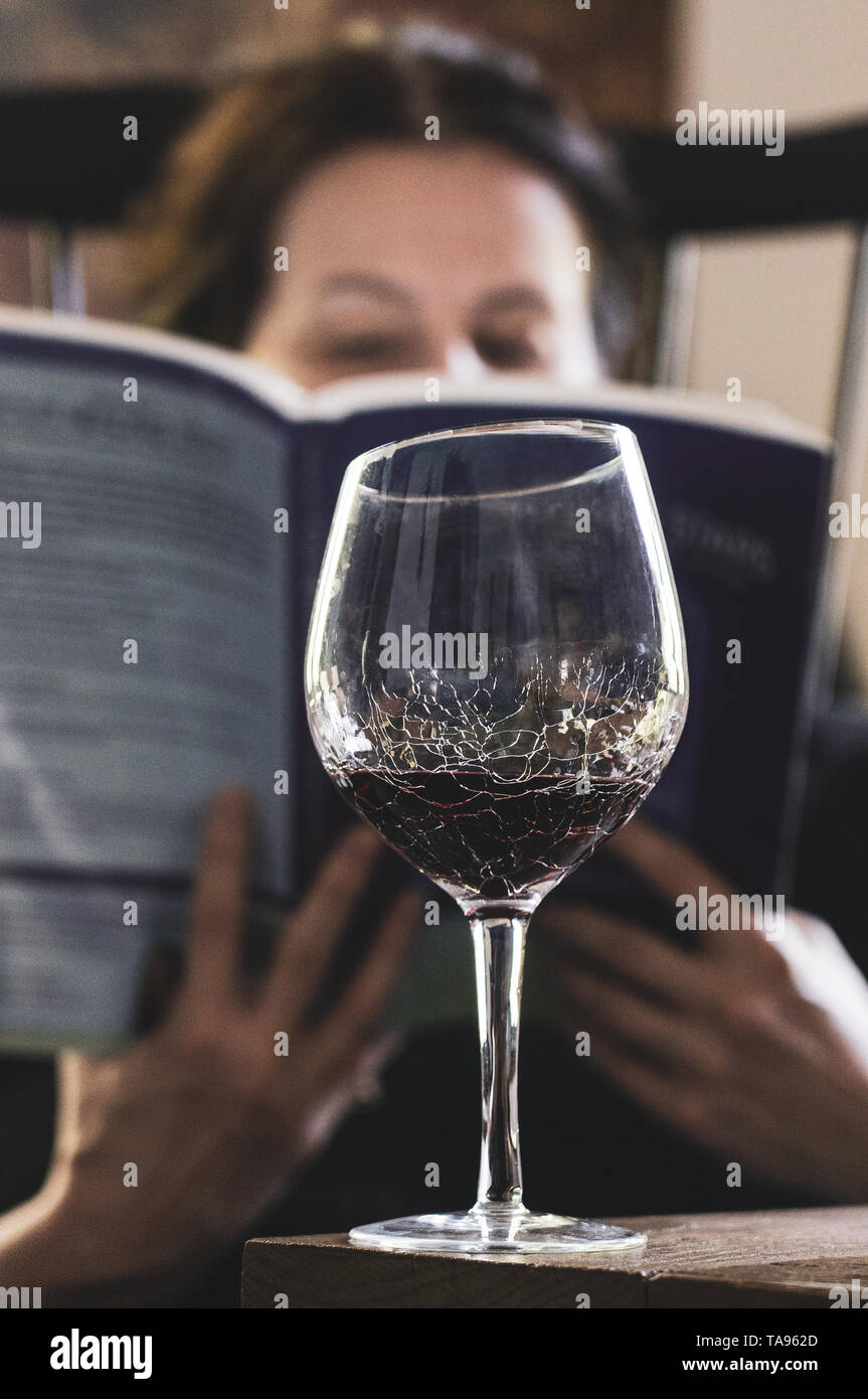 middle aged woman reads a book with a glass of wine Stock Photo