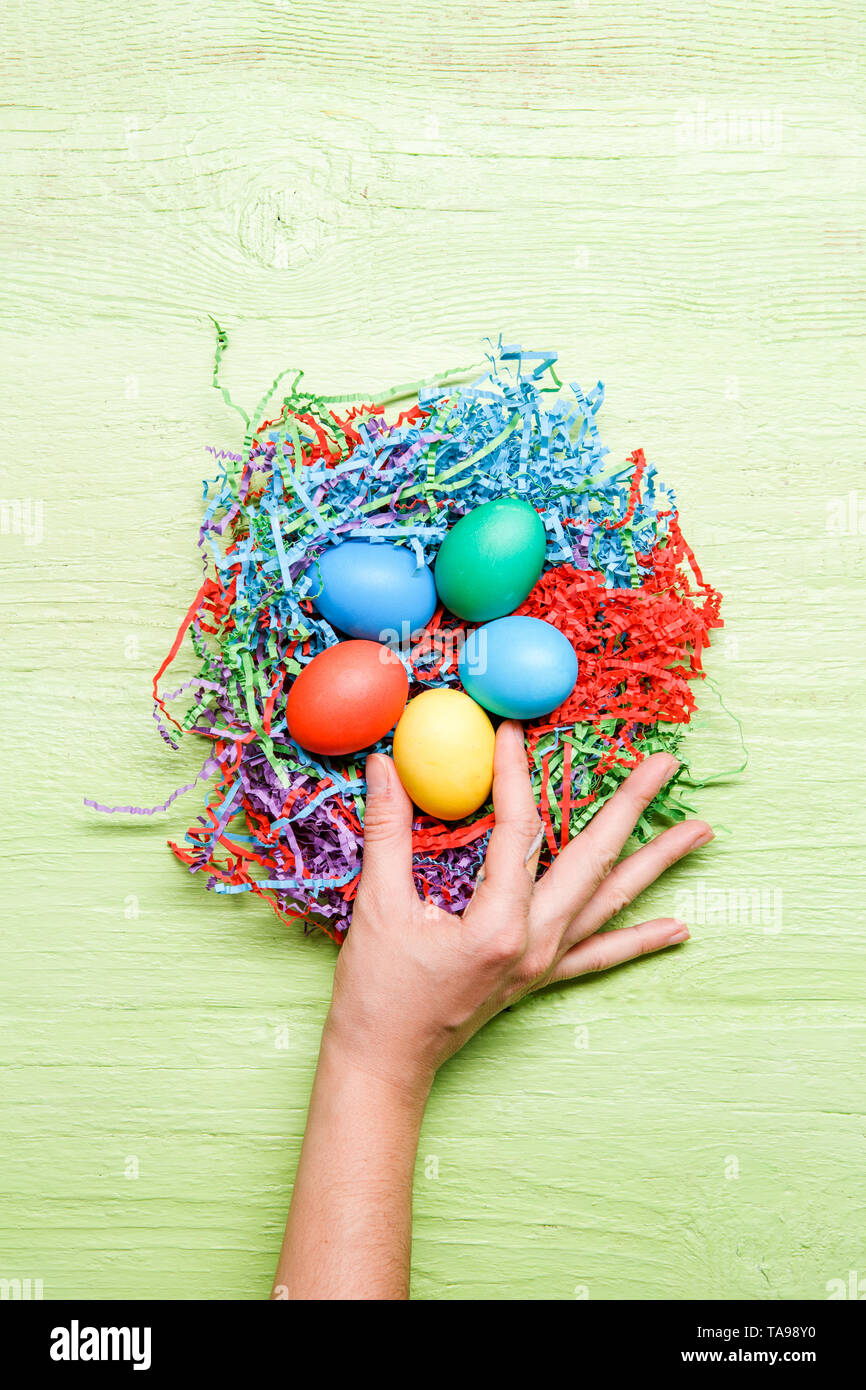 Photo of multicolored easter eggs and hand on green wooden background Stock Photo