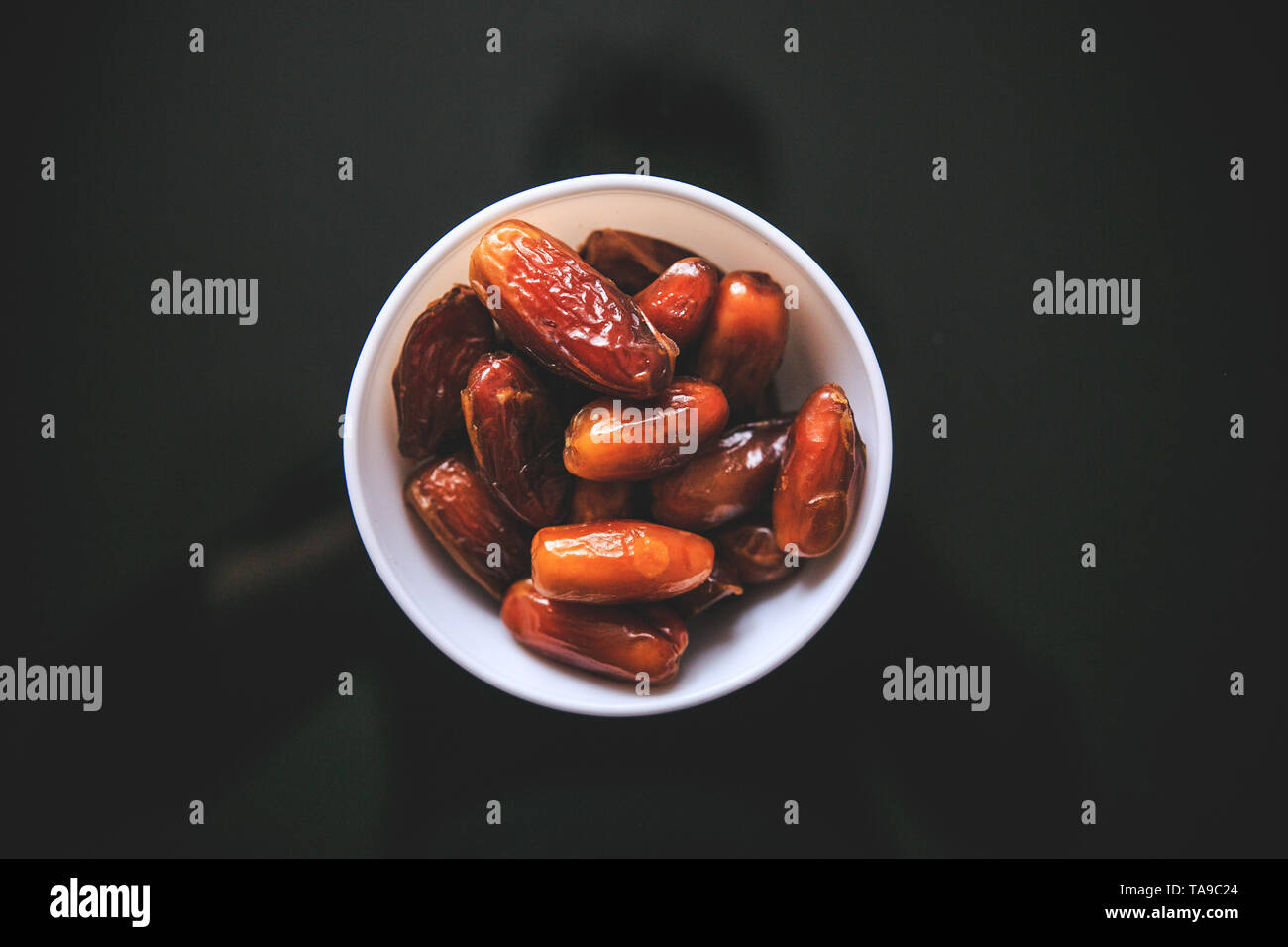 Dried whole dates in the white bowl holding in hand taken from the top on a black background. Stock Photo