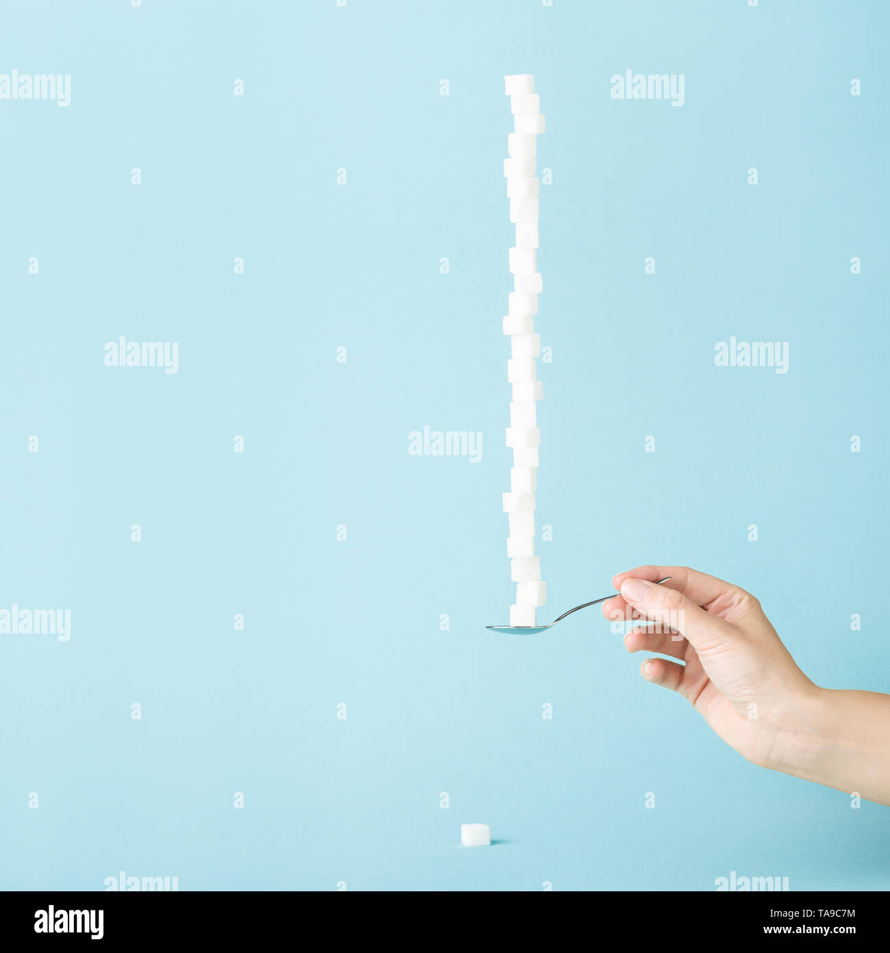 Female hand holding a spoon with column made of sugar cubes. Sweet life concept, minimal style. Sugar offering. Stock Photo