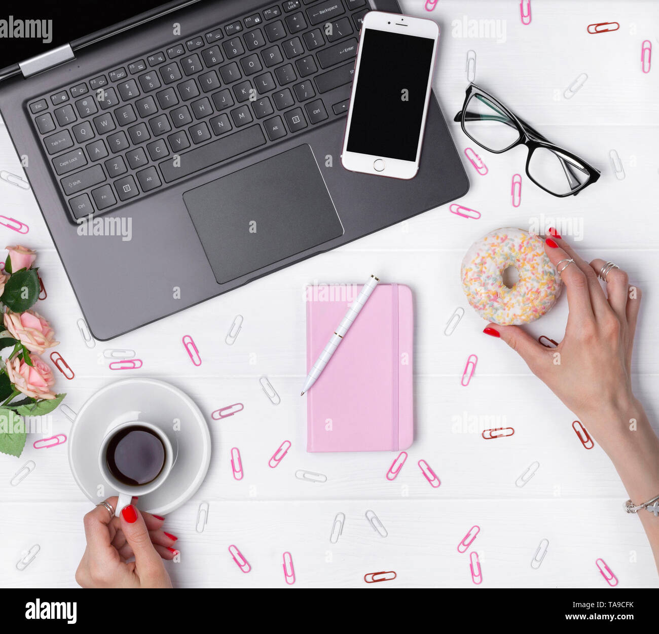 Female hands holding cup of coffee and donut while working on office ...