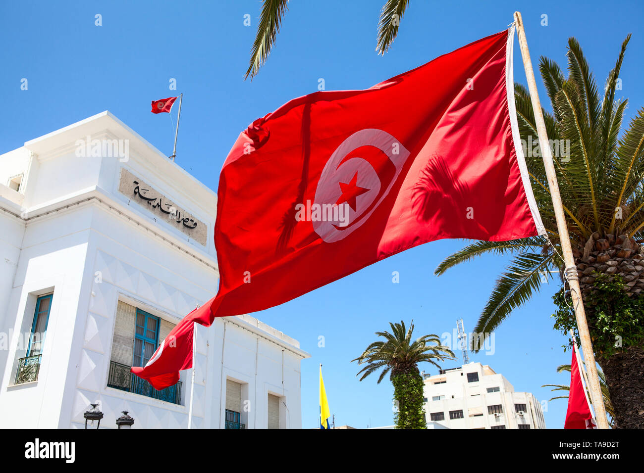 Red Tunisian national flag waves against administrative building in Sousse city. All government buildings must have flags on facade. Tunisia, the Afri Stock Photo