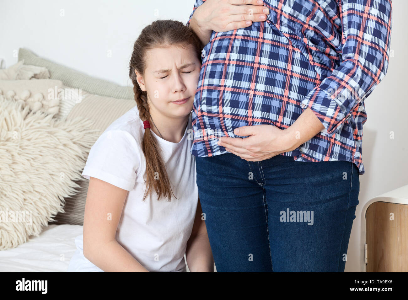 Young girl is not happy about new sibling, closing eyes and sobbing along her pregnant mother Stock Photo