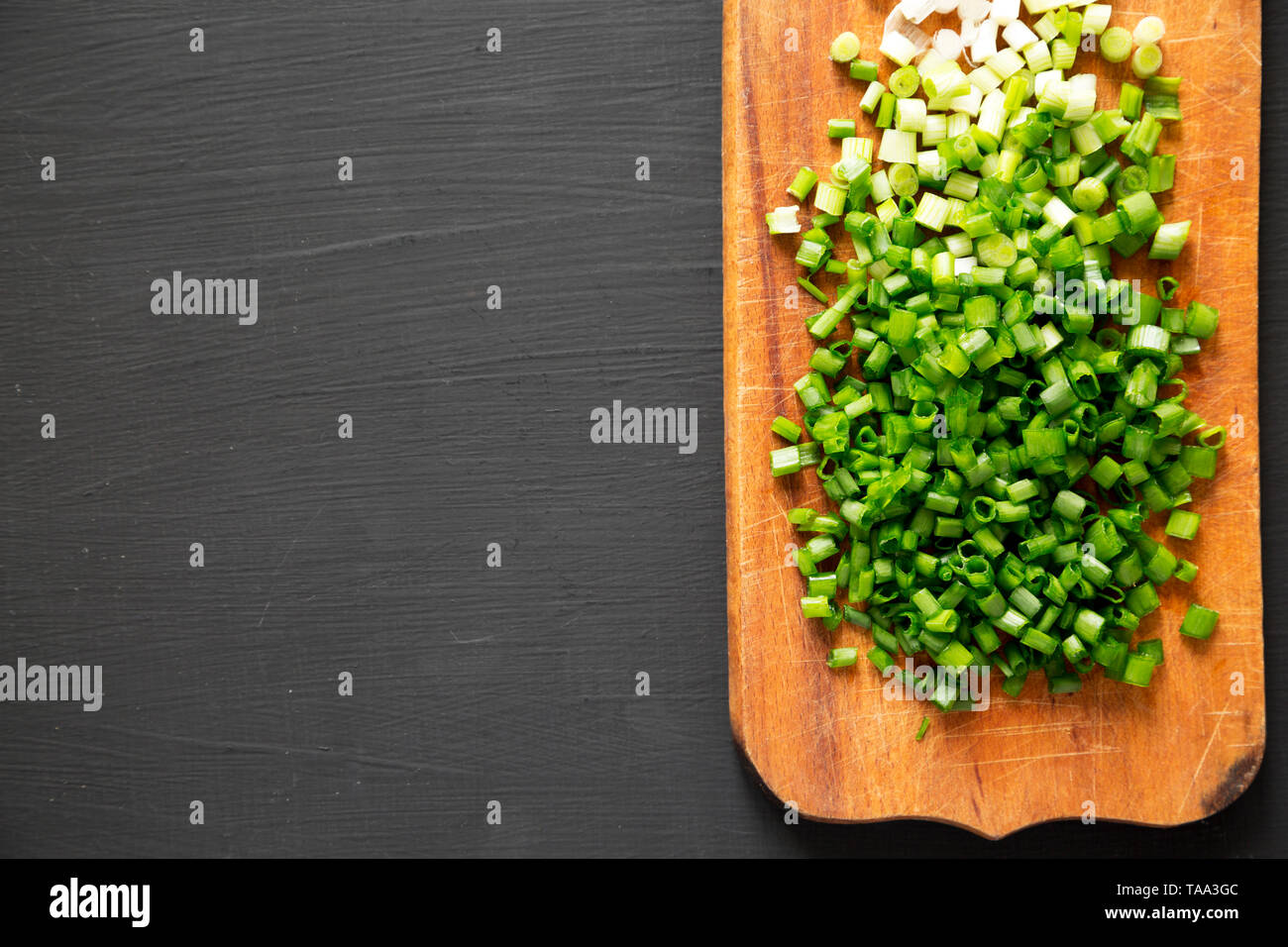 Chopped green onions on a rustic wooden board on a black surface, top ...