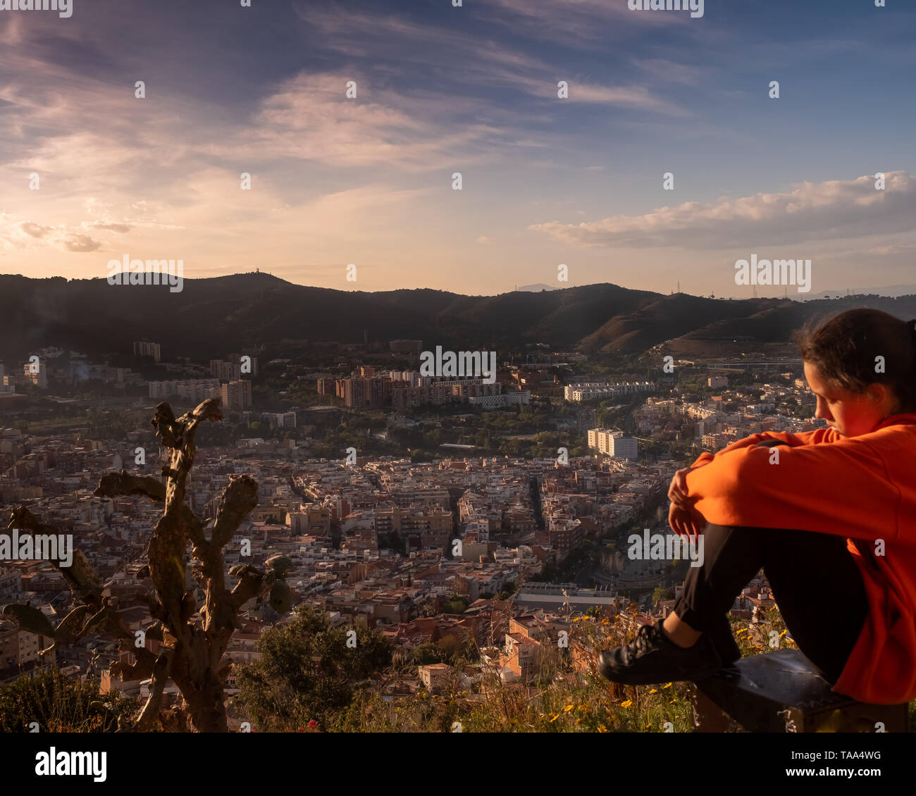 Sad girl sitting on the hill embracing her knees and looking away at sunset, sadly depressed teenager spending time alone, thoughtful teen feeling Stock Photo