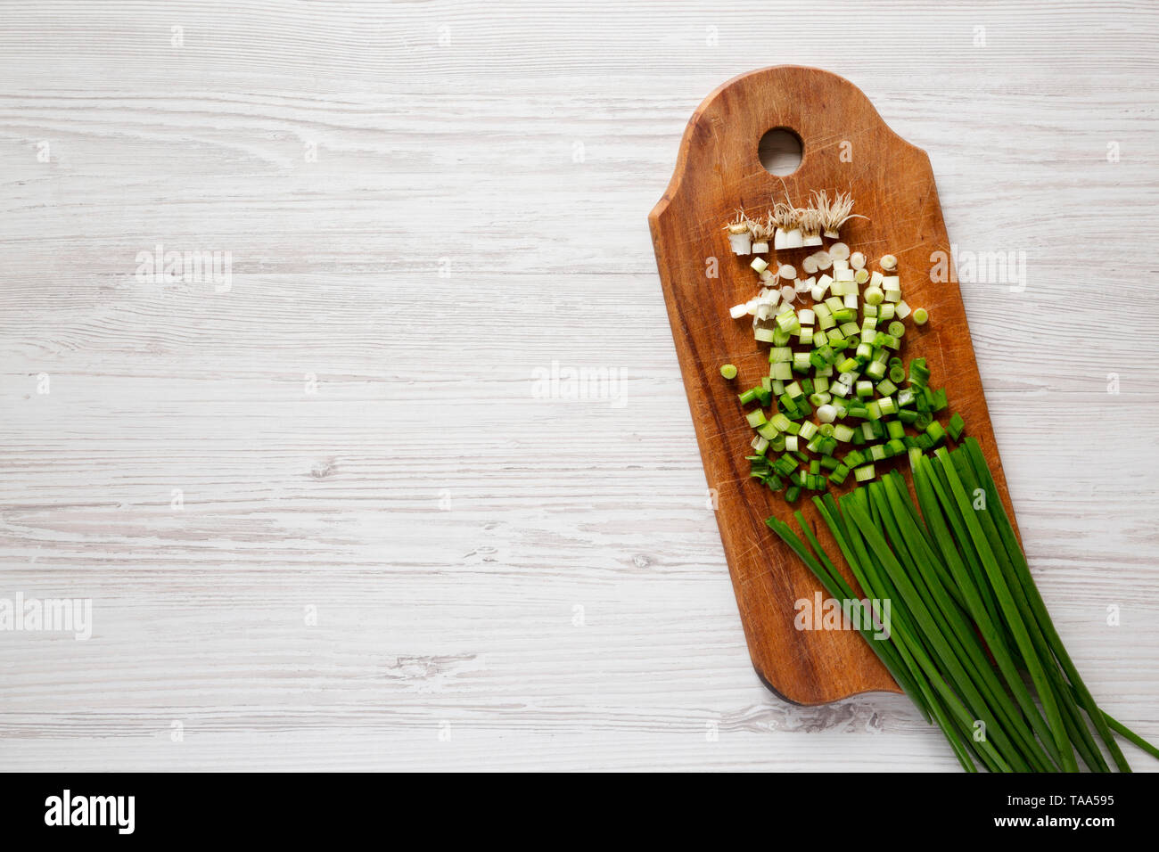 Chopped green onions on a rustic wooden board over white wooden surface ...