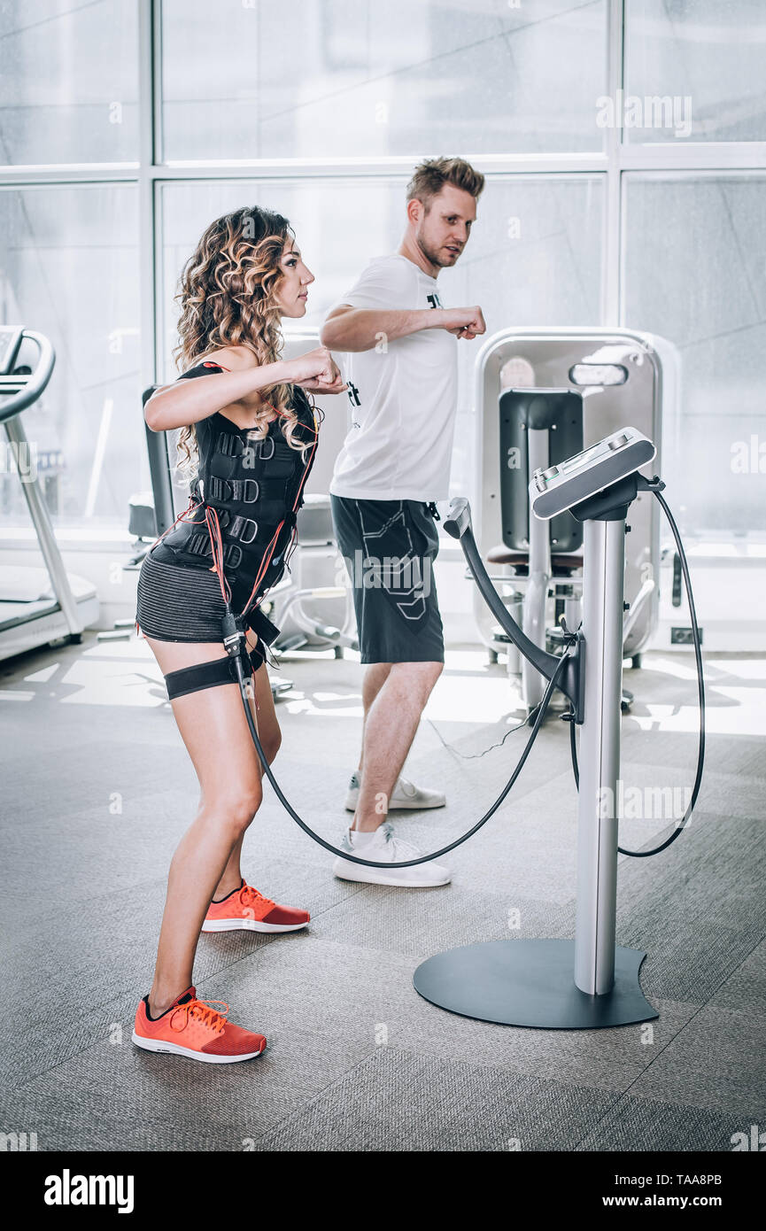 EMS electro stimulation women exercises with coach in modern gym