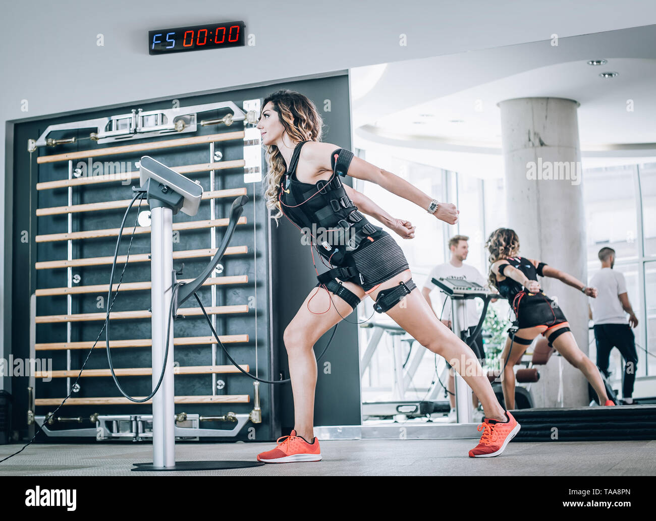 EMS electro stimulation women exercises with coach in modern gym. Electric muscle stimulation workout Stock Photo