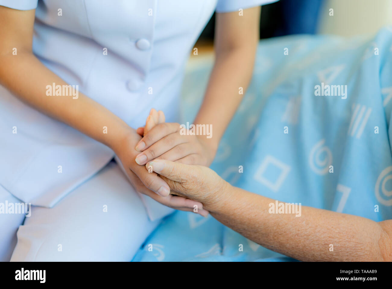 Nurse sitting on a hospital bed next to an older woman helping hands