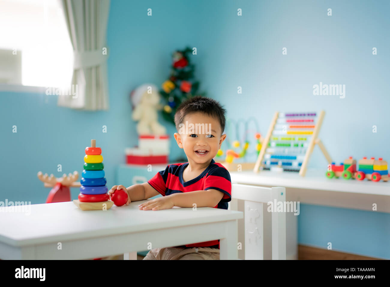 Adorable Asian Toddler baby boy sitting on chair and playing with color developmental toys at home. Stock Photo
