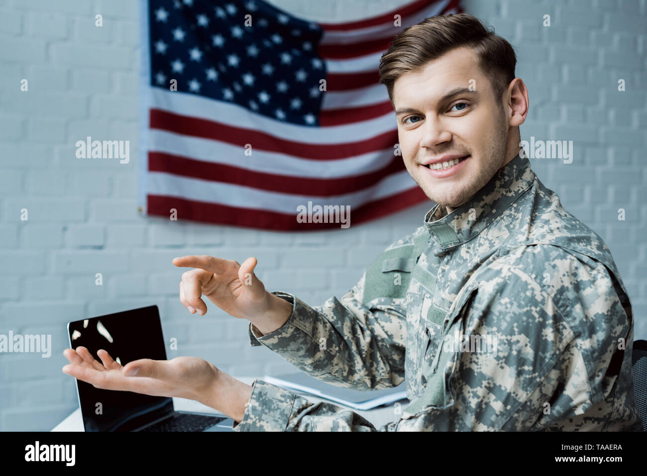 happy military man gesturing in office near laptop with blank screen ...