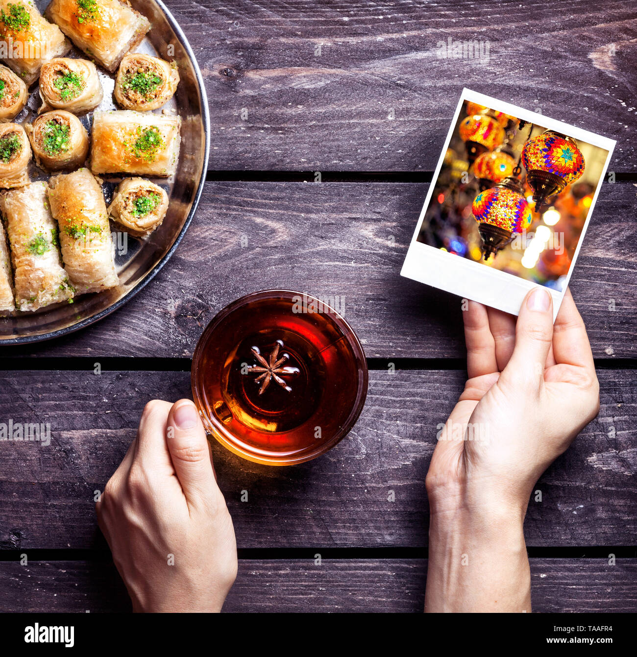 Hands with photo of oriental lantern in Istanbul grand market and black tea near Turkish baklava on wooden background Stock Photo