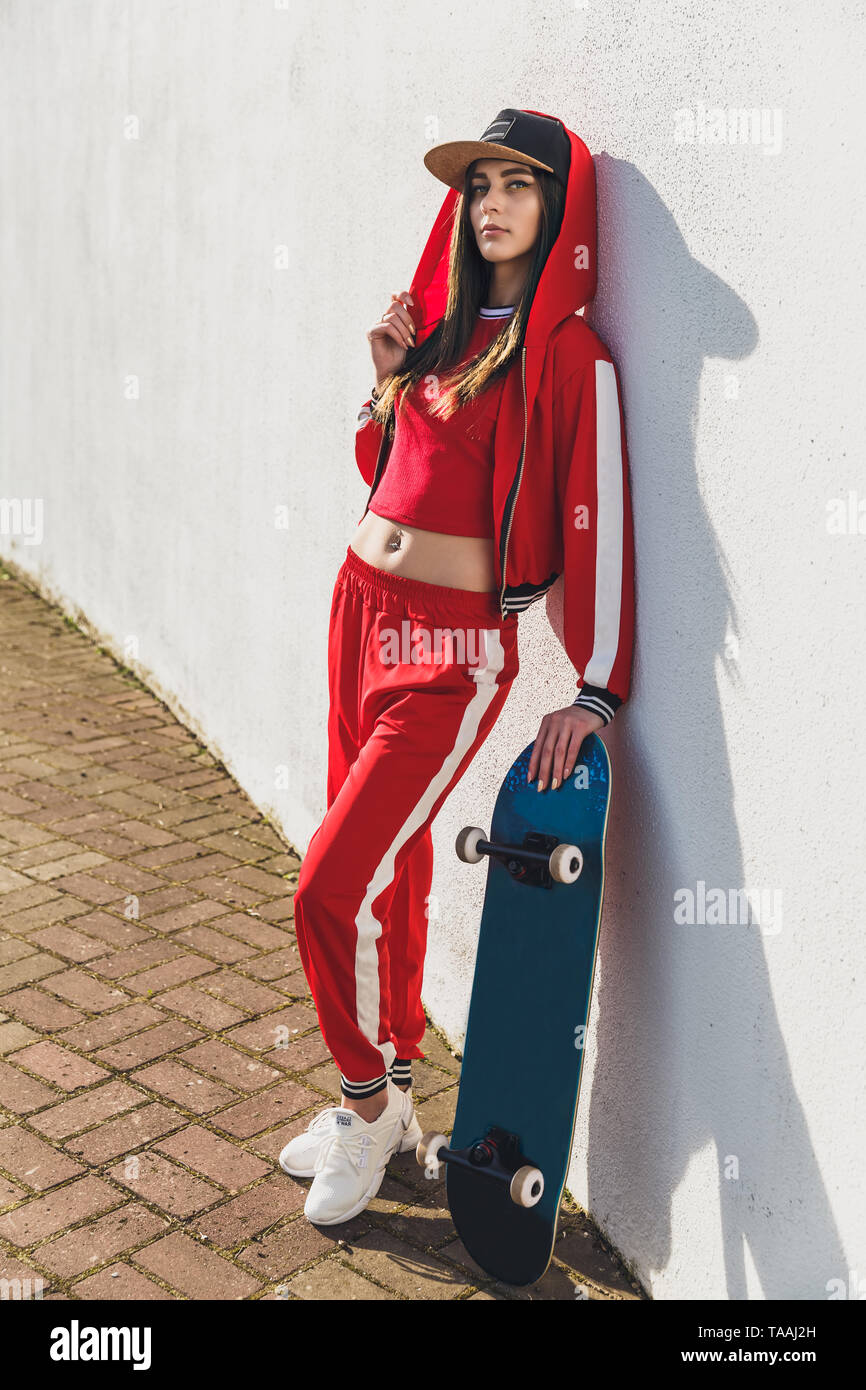 Portrait of young female wearing black hat, red clothing skateboarder  holding her skateboard. Woman with skating board looking at camera outdoors  Stock Photo - Alamy