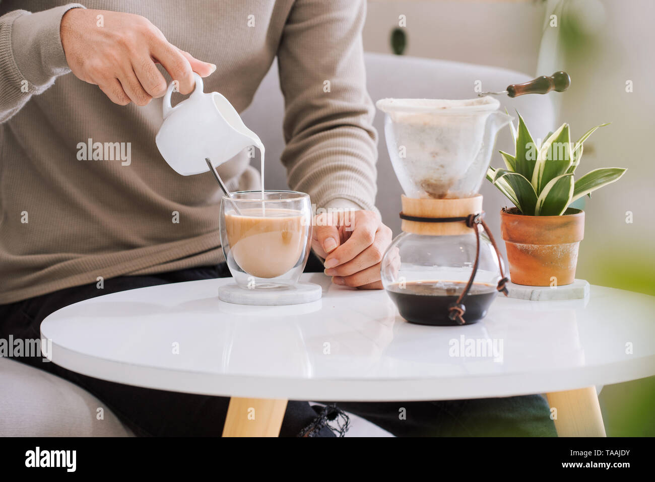 Coffee DRINK : man's hand pouring milk into a glass of espresso coffee in living room. Stock Photo