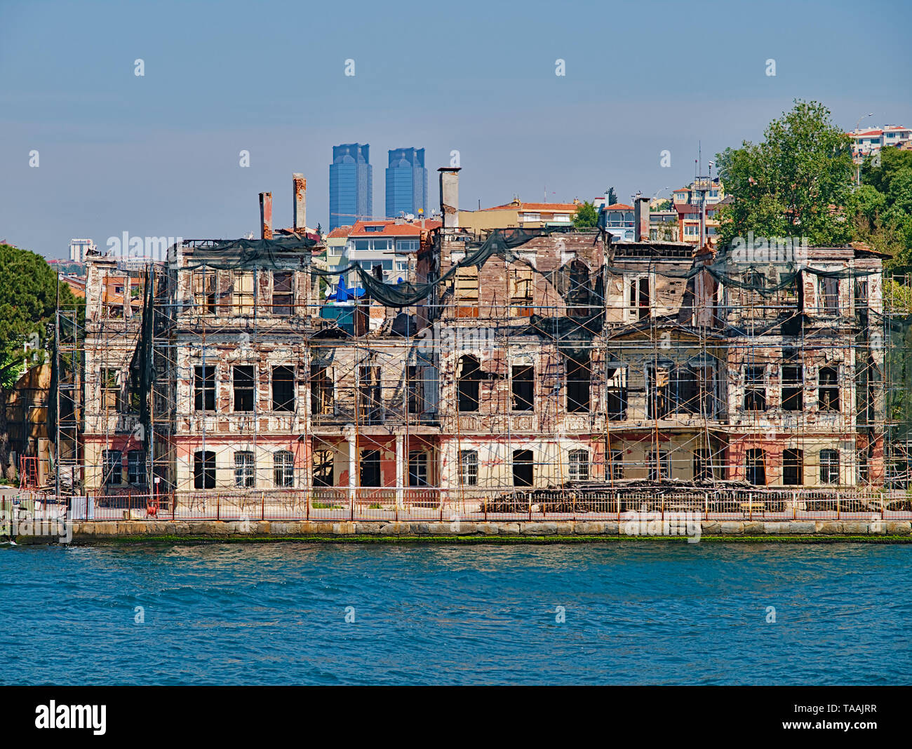 Bosporus strait, view from cruise ship. Old traditional damaged wooden building with structural support and TAT twin towers at the background. Stock Photo