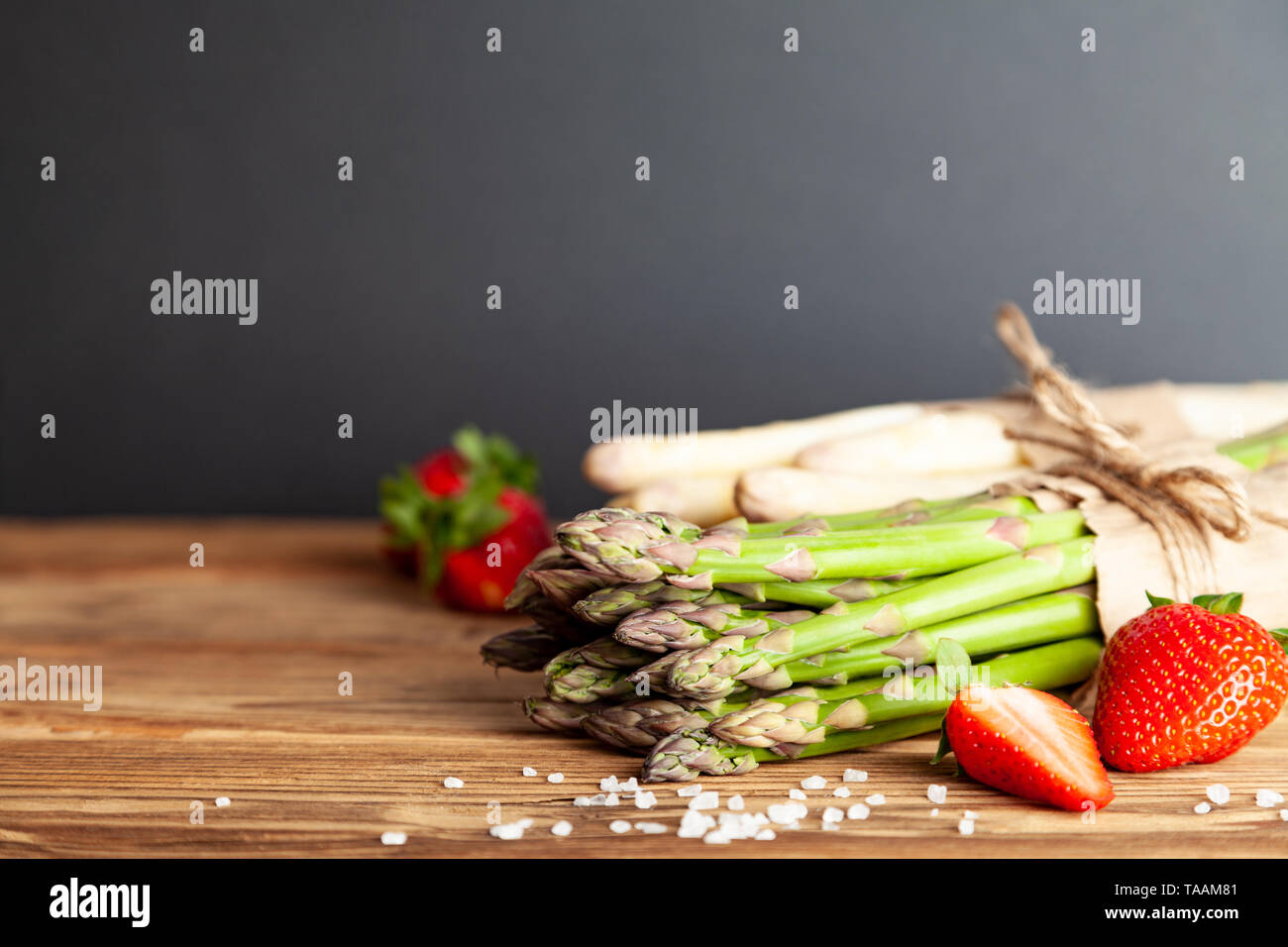 Fresh green and white asparagus with strawberries on rustic wooden table Stock Photo