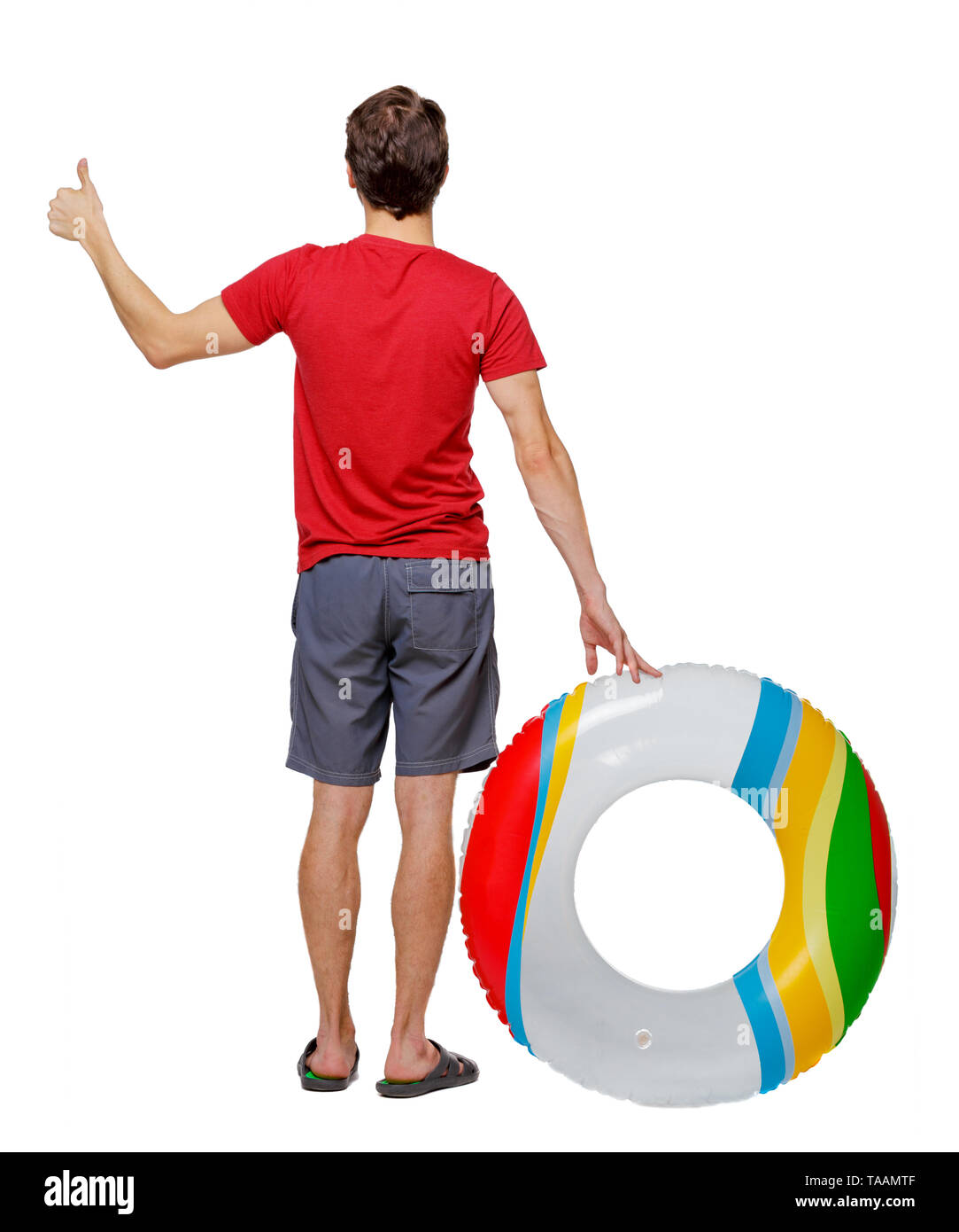 Back view of a man in shorts with an inflatable circle showing thumb up. The guy on the beach. Rear view people collection.  backside view of person.  Stock Photo